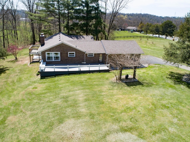 exterior space featuring brick siding, a wooden deck, a front yard, a chimney, and a forest view