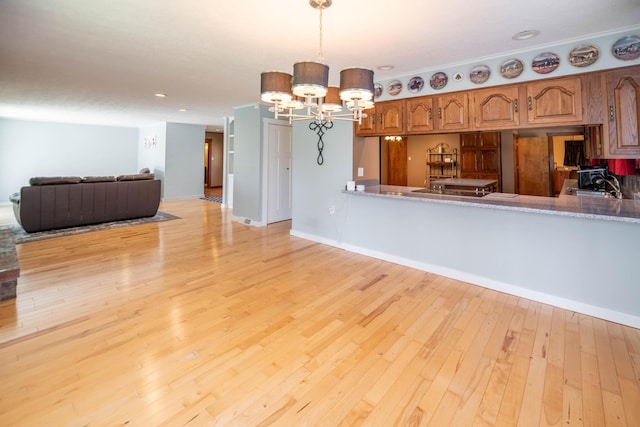 kitchen featuring brown cabinetry, pendant lighting, a sink, light wood finished floors, and an inviting chandelier