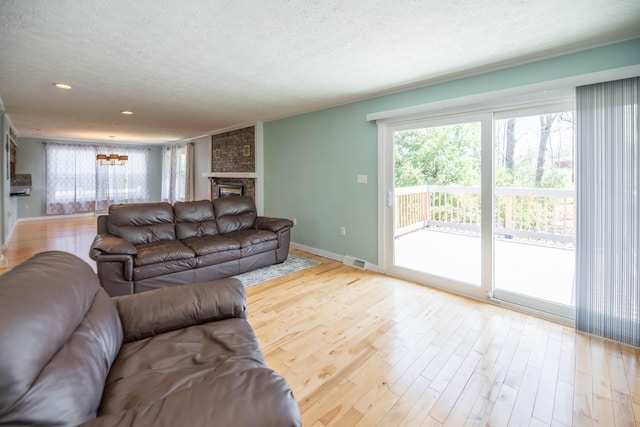 living room with visible vents, wood finished floors, baseboards, a stone fireplace, and a textured ceiling
