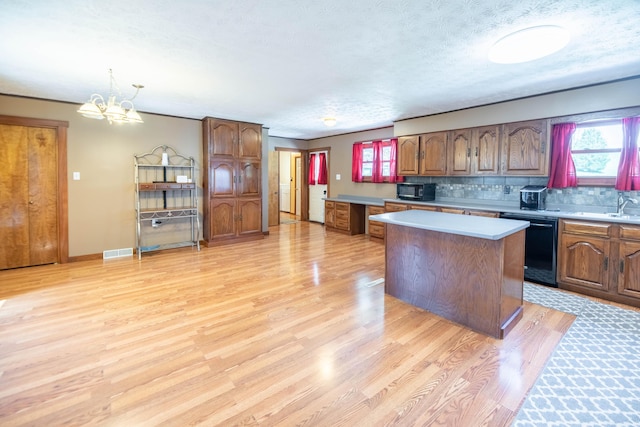 kitchen featuring decorative backsplash, a center island, light countertops, black appliances, and light wood-style flooring