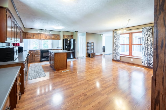 kitchen with brown cabinetry, light wood-style floors, a center island, a textured ceiling, and black appliances