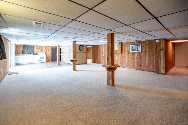 finished basement featuring carpet floors, wood walls, a paneled ceiling, and visible vents