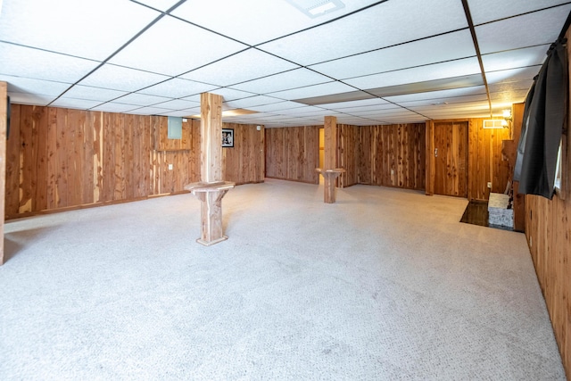 finished basement with wooden walls, carpet flooring, and a drop ceiling