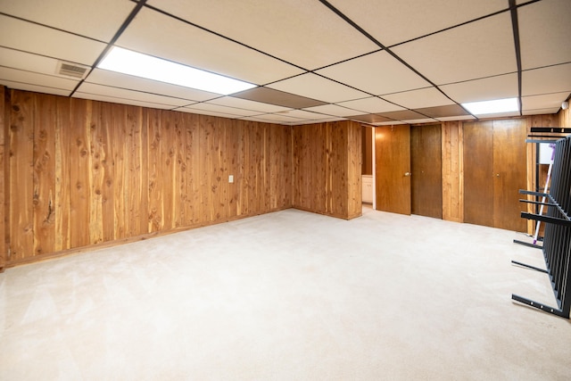 finished basement featuring carpet, a drop ceiling, wood walls, and visible vents