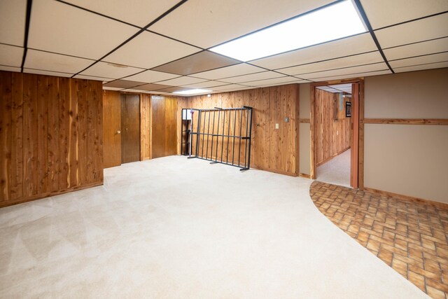 finished basement featuring wooden walls, a paneled ceiling, and carpet