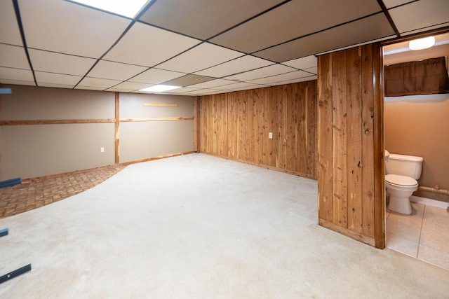 finished basement with wooden walls, baseboards, carpet flooring, and a paneled ceiling