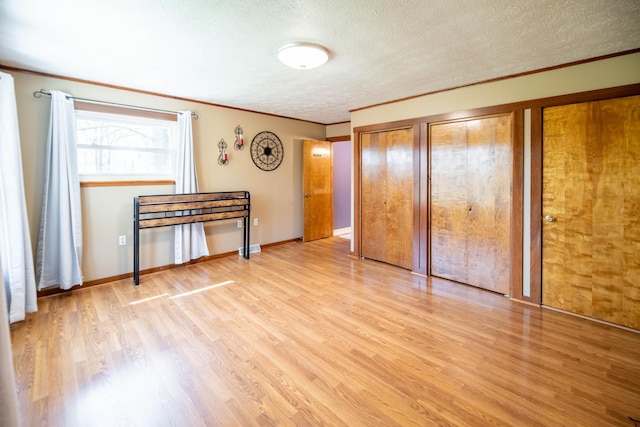 unfurnished bedroom featuring crown molding, two closets, baseboards, a textured ceiling, and light wood-style flooring