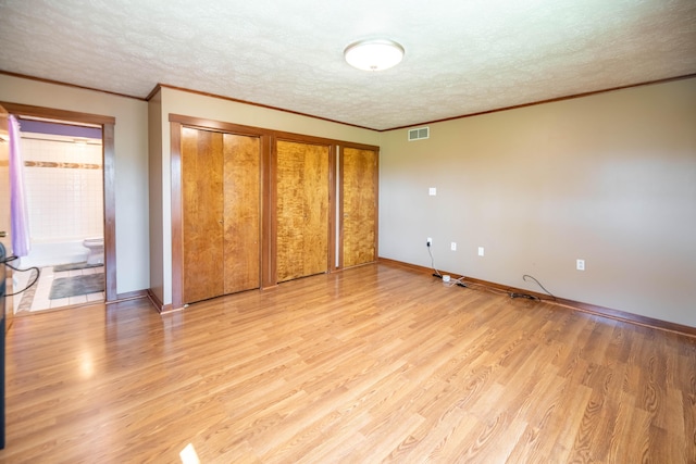 unfurnished bedroom with a textured ceiling, visible vents, crown molding, baseboards, and light wood-style flooring