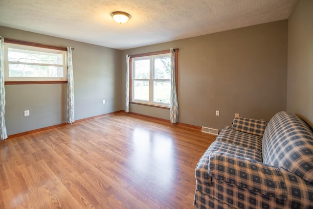 living area with a textured ceiling, baseboards, light wood-style flooring, and visible vents