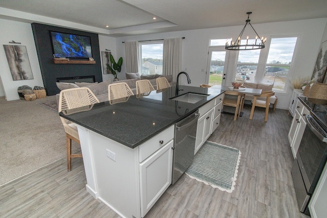 kitchen with open floor plan, white cabinets, a kitchen island with sink, dishwasher, and a sink