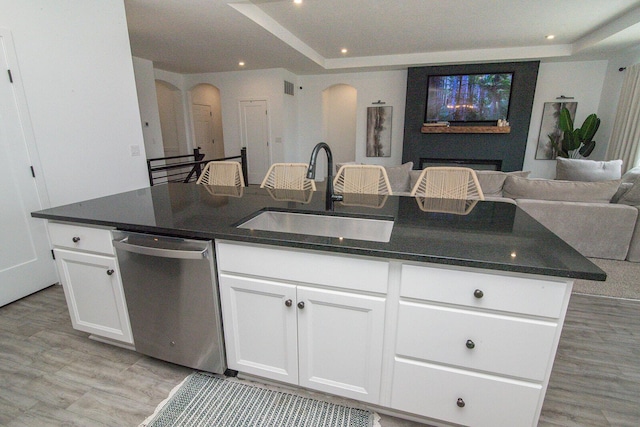 kitchen featuring arched walkways, a sink, open floor plan, white cabinetry, and stainless steel dishwasher