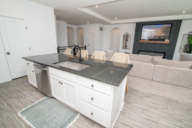 kitchen featuring an island with sink, arched walkways, light wood finished floors, dishwasher, and a sink