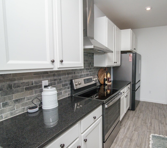 kitchen featuring dark stone countertops, wall chimney range hood, white cabinetry, stainless steel appliances, and backsplash