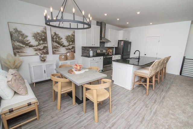 kitchen with wall chimney exhaust hood, stainless steel range with electric stovetop, a sink, freestanding refrigerator, and dark countertops