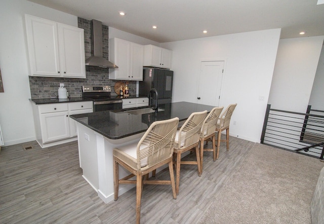 kitchen featuring freestanding refrigerator, electric range, wall chimney range hood, dark countertops, and a sink