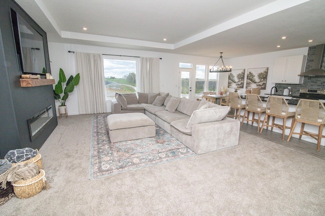 living room featuring a large fireplace, a raised ceiling, an inviting chandelier, and recessed lighting