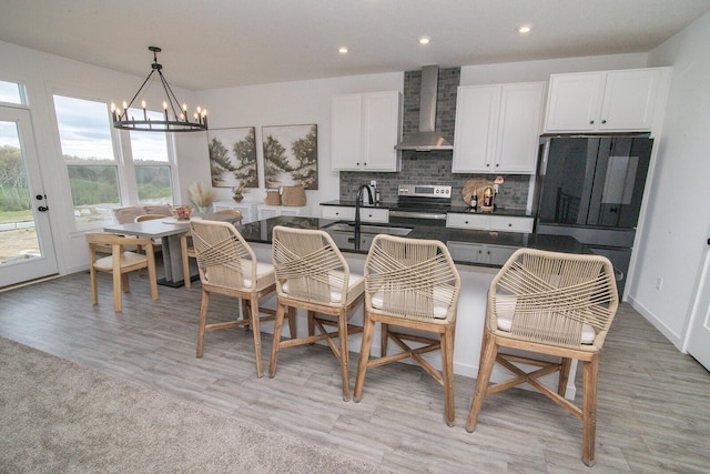 kitchen with a notable chandelier, dark countertops, stainless steel range with electric stovetop, wall chimney exhaust hood, and fridge