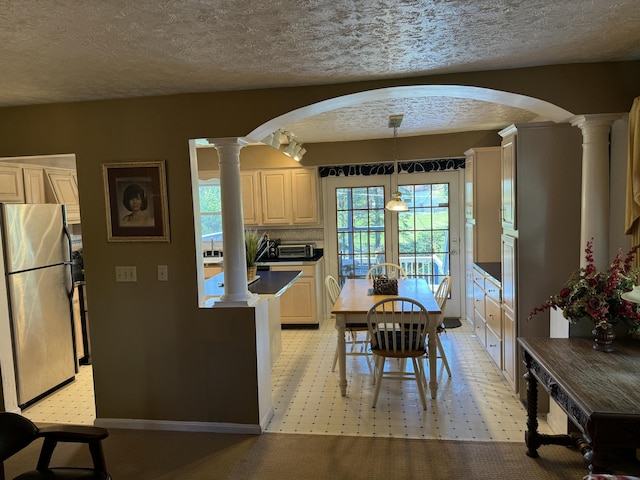 kitchen featuring decorative columns, arched walkways, a textured ceiling, and freestanding refrigerator