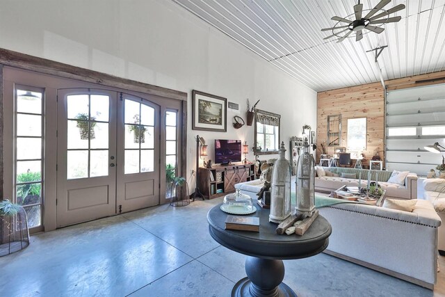 foyer with ceiling fan, concrete floors, wood walls, and french doors