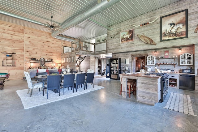 dining space featuring wood walls, a towering ceiling, finished concrete flooring, and ceiling fan
