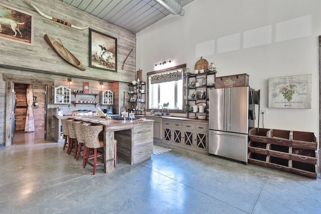 kitchen featuring a towering ceiling, open shelves, a sink, freestanding refrigerator, and concrete floors
