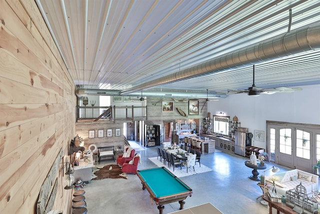 living area featuring a ceiling fan, wood walls, and finished concrete floors