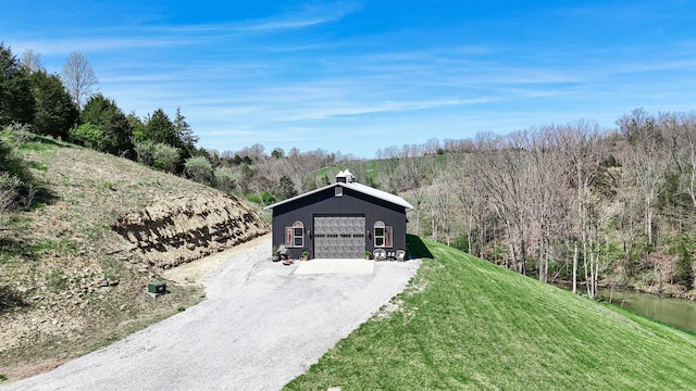 view of front facade featuring gravel driveway, an outbuilding, a wooded view, a detached garage, and a front yard
