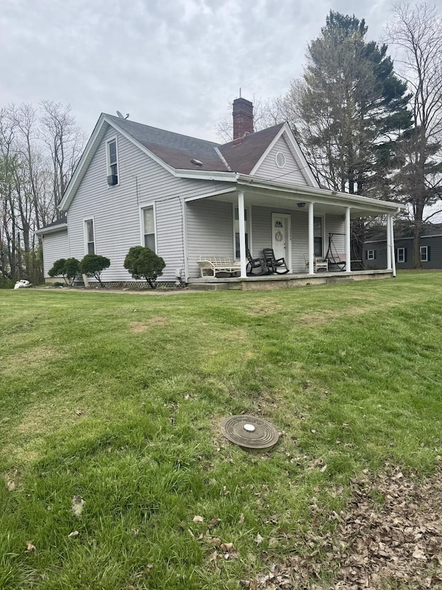 back of house featuring a chimney, covered porch, and a yard