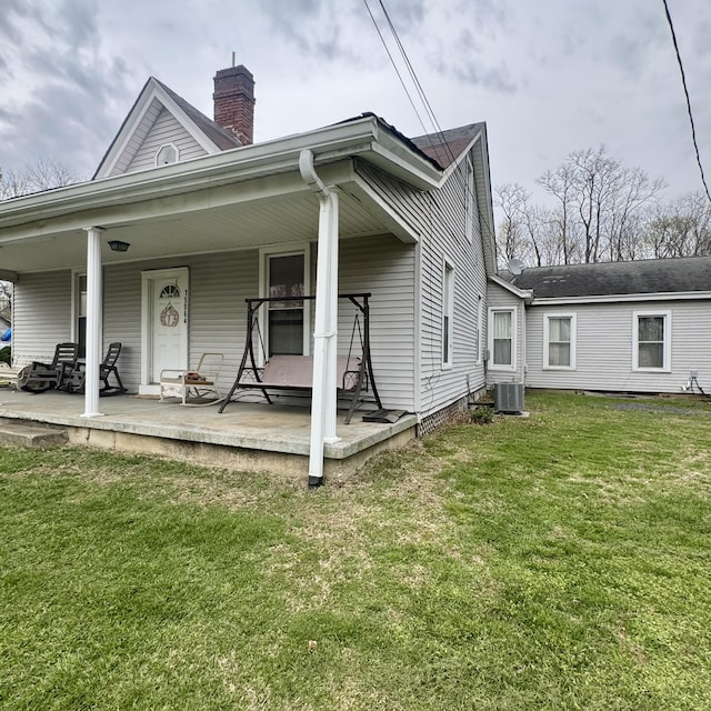 view of front of property with central air condition unit, a chimney, a front yard, and covered porch