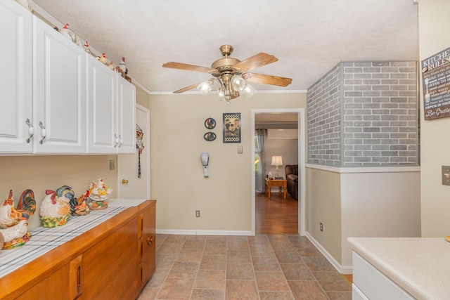 kitchen with a ceiling fan, tile counters, white cabinets, baseboards, and stone finish floor