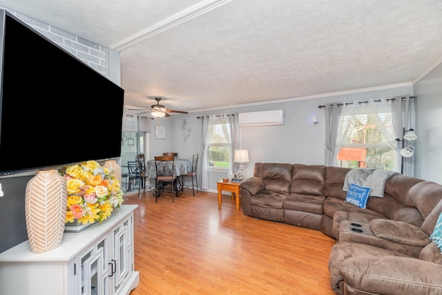 living room featuring an AC wall unit, a ceiling fan, ornamental molding, light wood-type flooring, and a textured ceiling