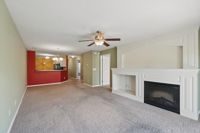 unfurnished living room with a glass covered fireplace, carpet floors, baseboards, and ceiling fan with notable chandelier