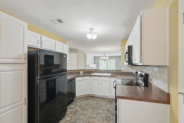 kitchen featuring stone finish floor, visible vents, dark countertops, black appliances, and a chandelier