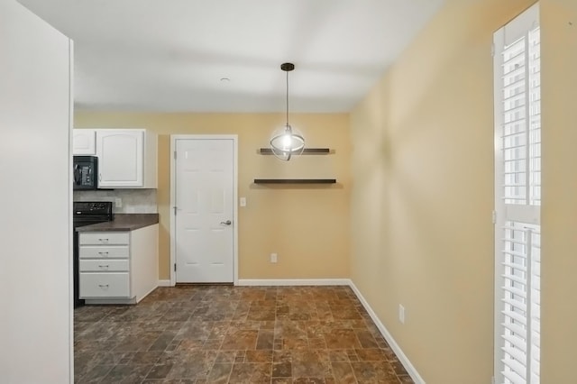 kitchen featuring stone finish flooring, black microwave, dark countertops, white cabinets, and a wealth of natural light