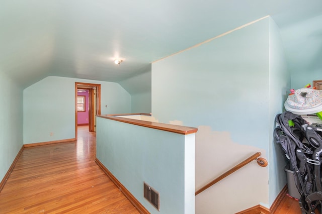 hall featuring vaulted ceiling, an upstairs landing, light wood-style flooring, and visible vents