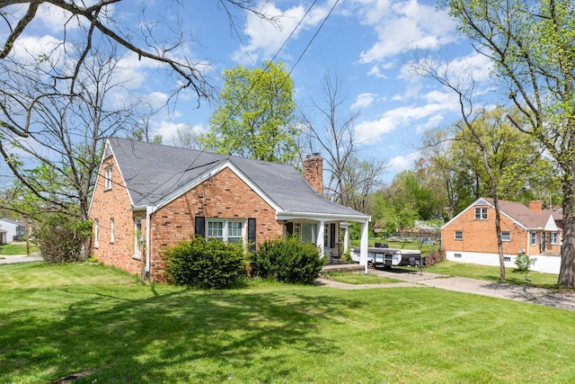 view of front of property featuring roof with shingles, brick siding, a porch, a front yard, and a chimney