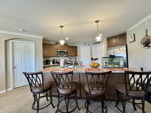 kitchen with light carpet, a kitchen bar, light countertops, appliances with stainless steel finishes, and hanging light fixtures