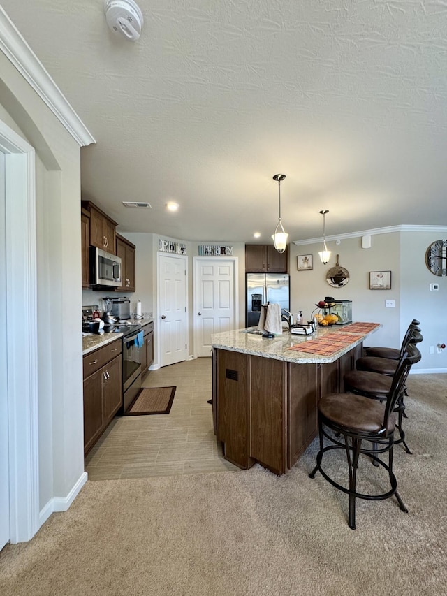 kitchen featuring a breakfast bar, dark brown cabinetry, appliances with stainless steel finishes, light colored carpet, and ornamental molding