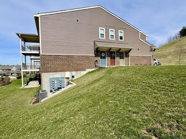 back of property featuring brick siding, a yard, central AC, and a balcony