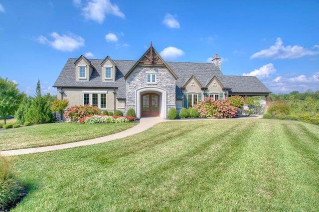 french country style house featuring a chimney, stone siding, a front yard, and french doors