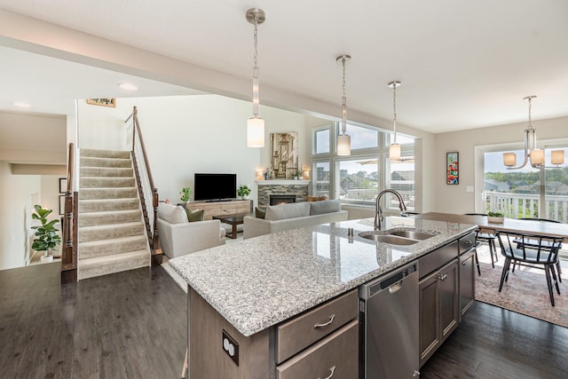 kitchen with stainless steel dishwasher, a stone fireplace, a sink, dark wood-style floors, and a notable chandelier