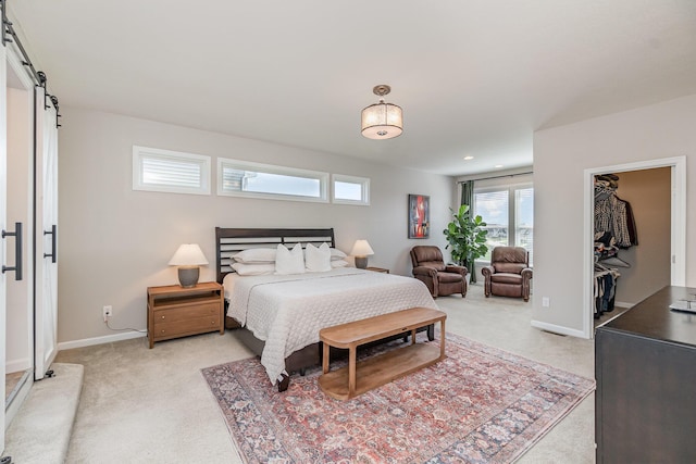 bedroom featuring baseboards, a barn door, a walk in closet, and light colored carpet