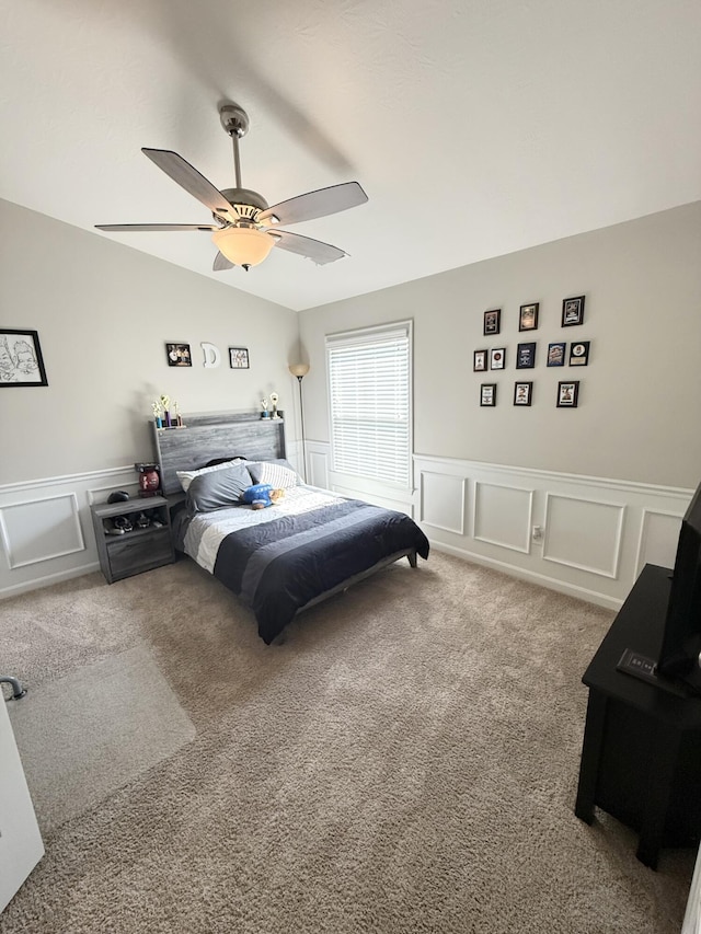 carpeted bedroom featuring wainscoting, ceiling fan, and a decorative wall