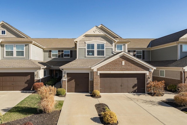townhome / multi-family property with a garage, a shingled roof, brick siding, and concrete driveway