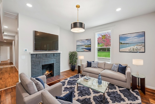 living room with wood finished floors, a brick fireplace, recessed lighting, and baseboards