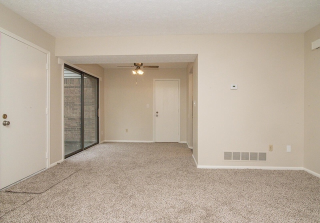 empty room with carpet flooring, ceiling fan, a textured ceiling, baseboards, and visible vents