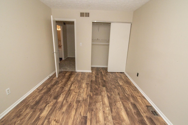 unfurnished bedroom with baseboards, visible vents, wood finished floors, and a closet