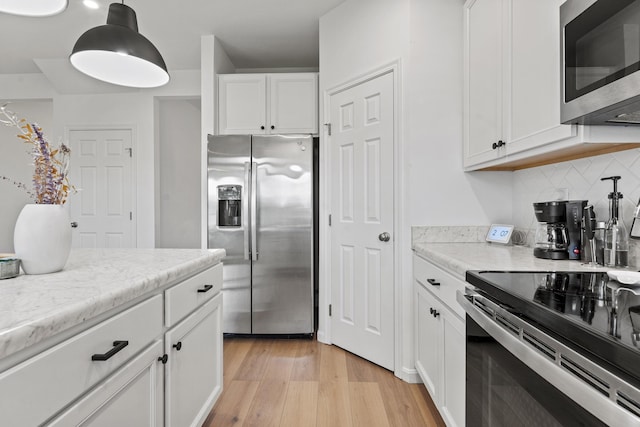 kitchen featuring white cabinets, stainless steel appliances, decorative light fixtures, decorative backsplash, and light wood-type flooring