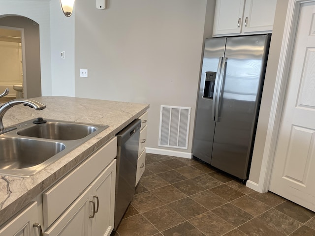 kitchen featuring stainless steel appliances, a sink, arched walkways, baseboards, and visible vents