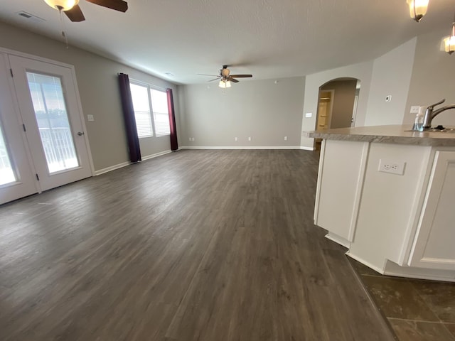 unfurnished living room with dark wood-style floors, arched walkways, a sink, visible vents, and a ceiling fan